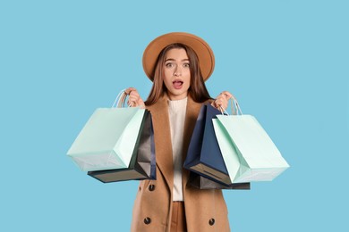 Photo of Surprised young woman with shopping bags on light blue background. Big sale