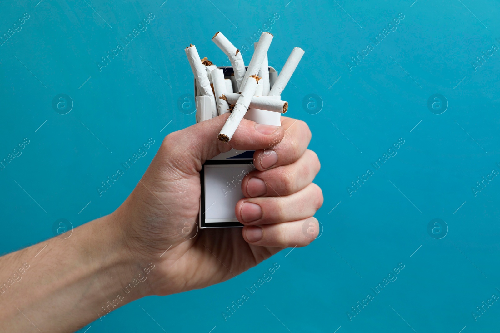 Photo of Stop smoking. Man holding pack with broken cigarettes on light blue background, closeup