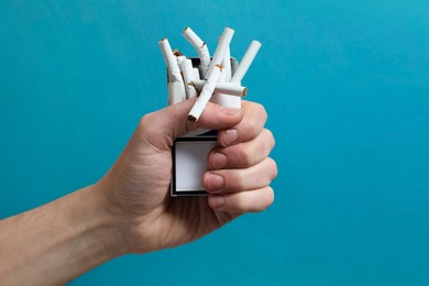 Photo of Stop smoking. Man holding pack with broken cigarettes on light blue background, closeup