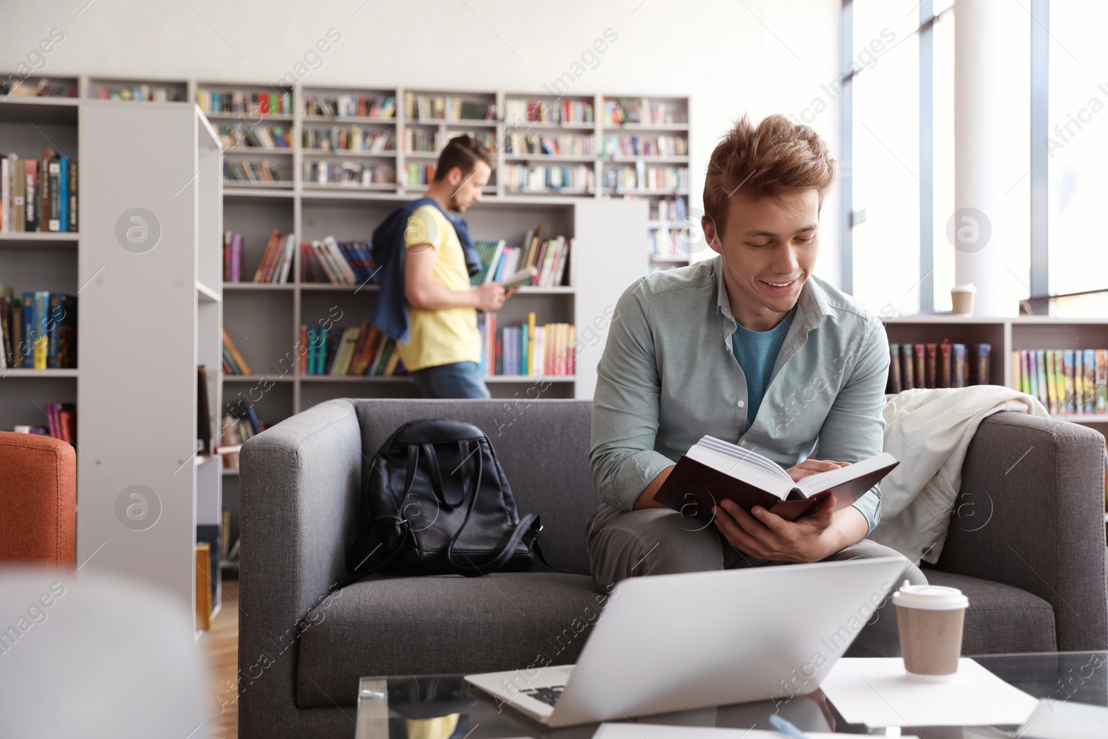 Photo of Young man studying on sofa in modern library