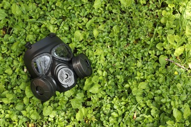 One gas mask on green grass outdoors, top view. Space for text