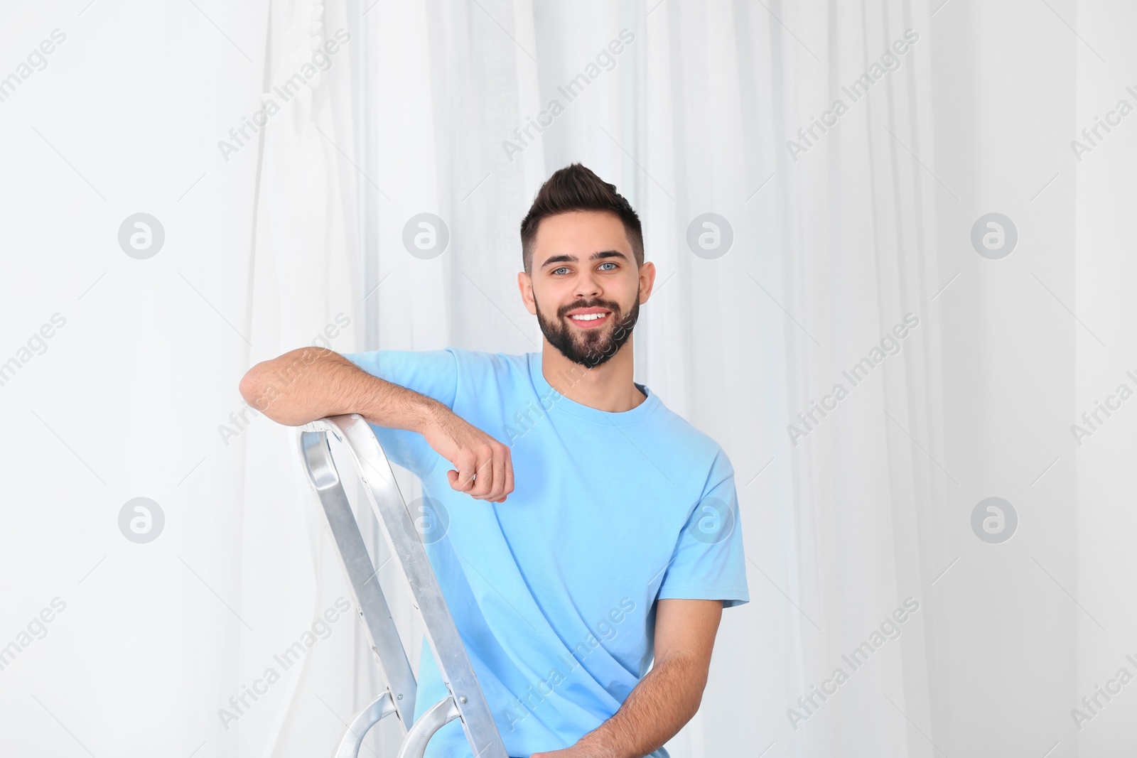 Photo of Young man sitting on stepladder near window with curtain in room
