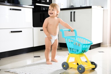 Photo of Cute baby with toy walker in kitchen. Learning to walk