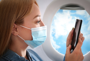 Traveling by airplane during coronavirus pandemic. Woman with face mask and phone near porthole