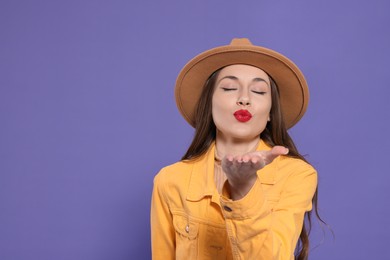 Beautiful young woman blowing kiss on purple background, space for text