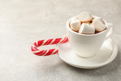 Photo of Tasty hot chocolate with marshmallows and candy cane on light grey table, closeup