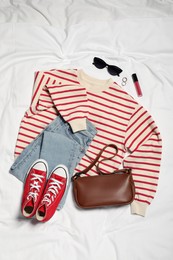 Pair of stylish red sneakers, clothes and accessories on white fabric, flat lay