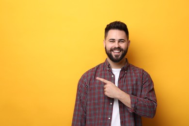 Happy young man with mustache pointing at something on yellow background. Space for text