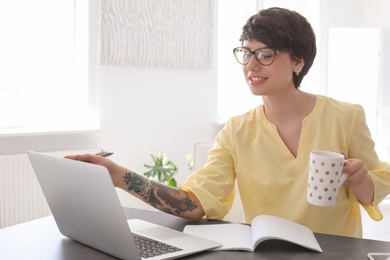 Photo of Young woman drinking coffee while working with laptop at desk. Home office