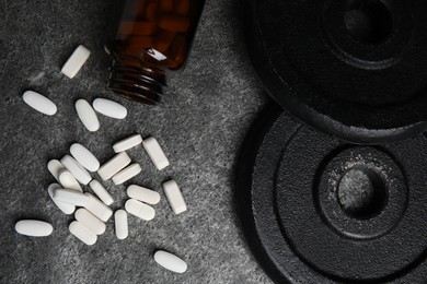 Bottle near amino acid pills and weight plates on grey table, flat lay