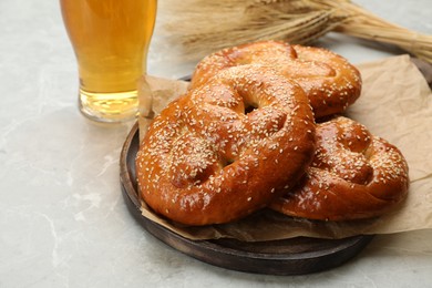 Tasty pretzels, glass of beer and wheat spikes on light grey table