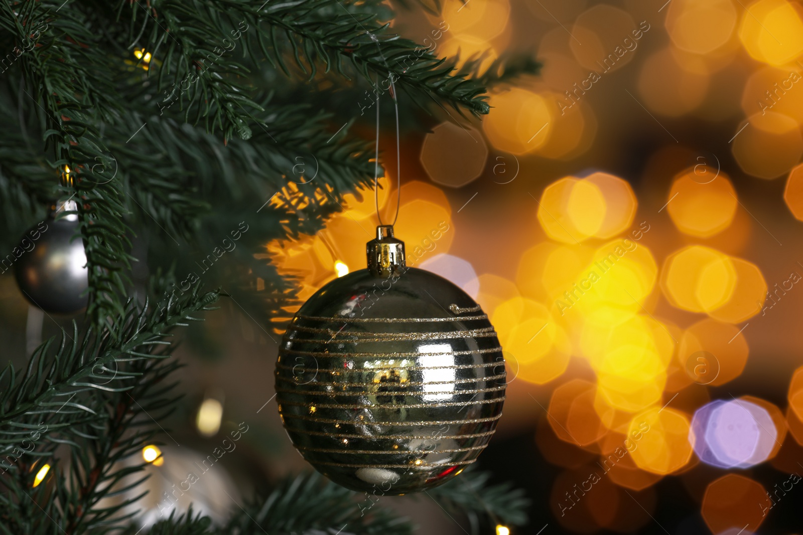 Photo of Beautiful shiny holiday bauble hanging on Christmas tree against blurred fairy lights, closeup. Space for text