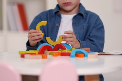 Photo of Little boy playing with colorful wooden pieces at white table indoors, closeup. Child's toy