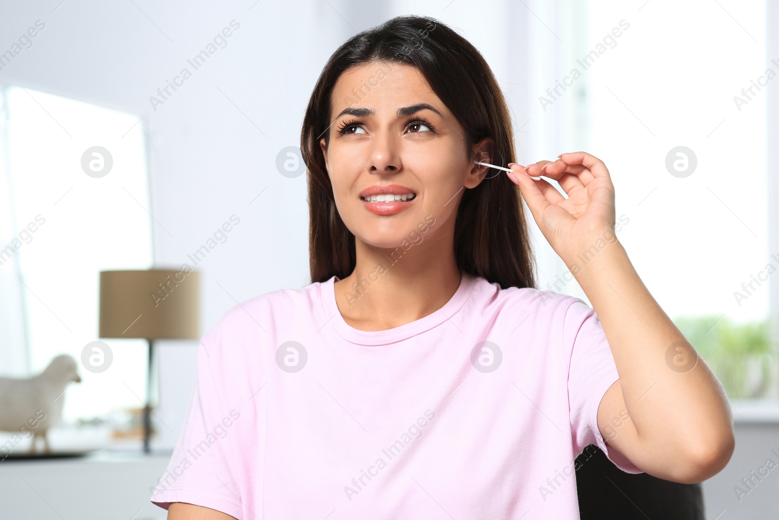 Photo of Young woman cleaning ear with cotton swab indoors