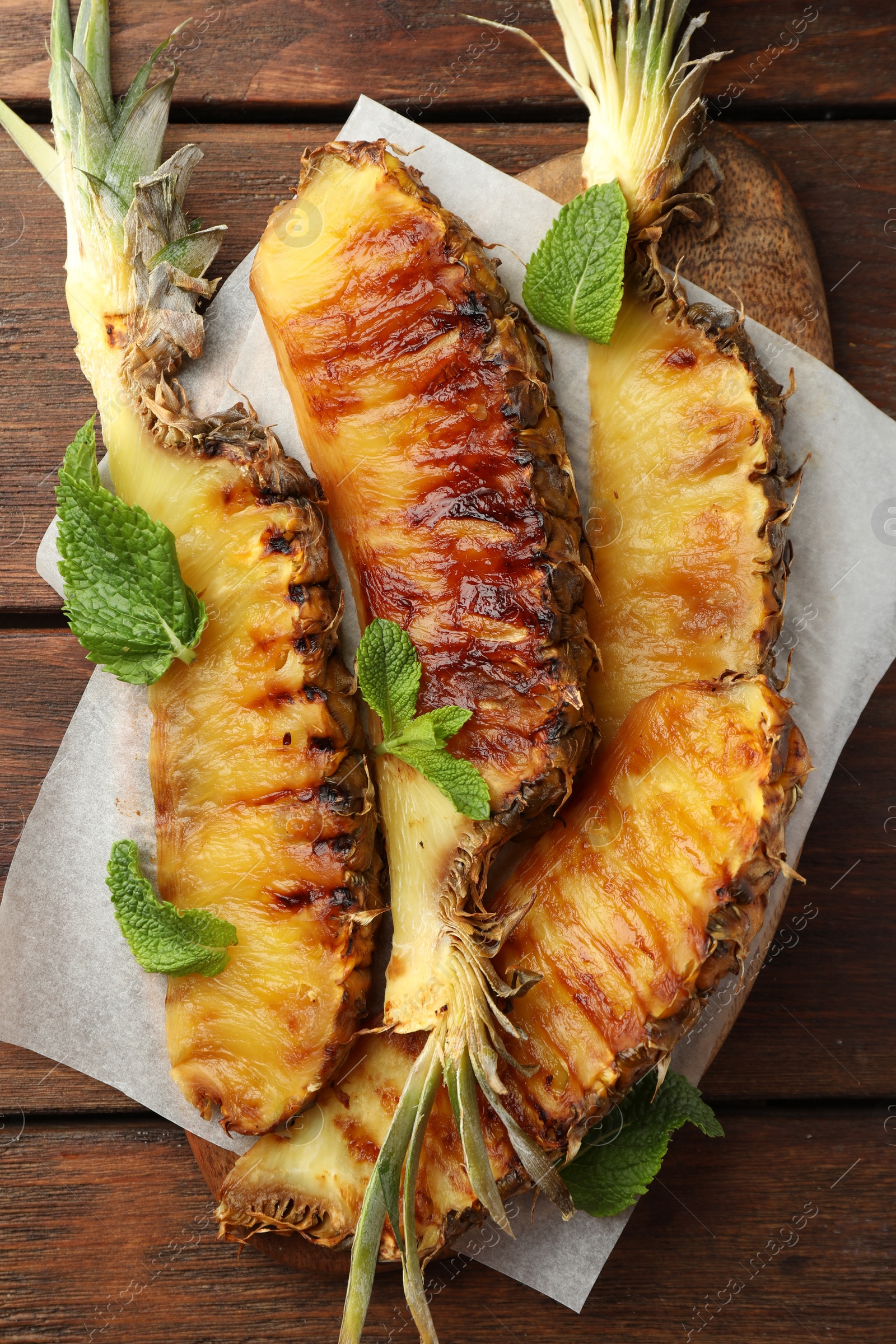 Photo of Tasty grilled pineapple pieces and mint leaves on wooden table, top view