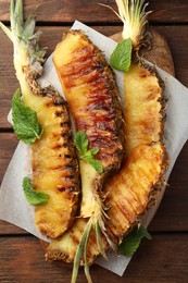Tasty grilled pineapple pieces and mint leaves on wooden table, top view