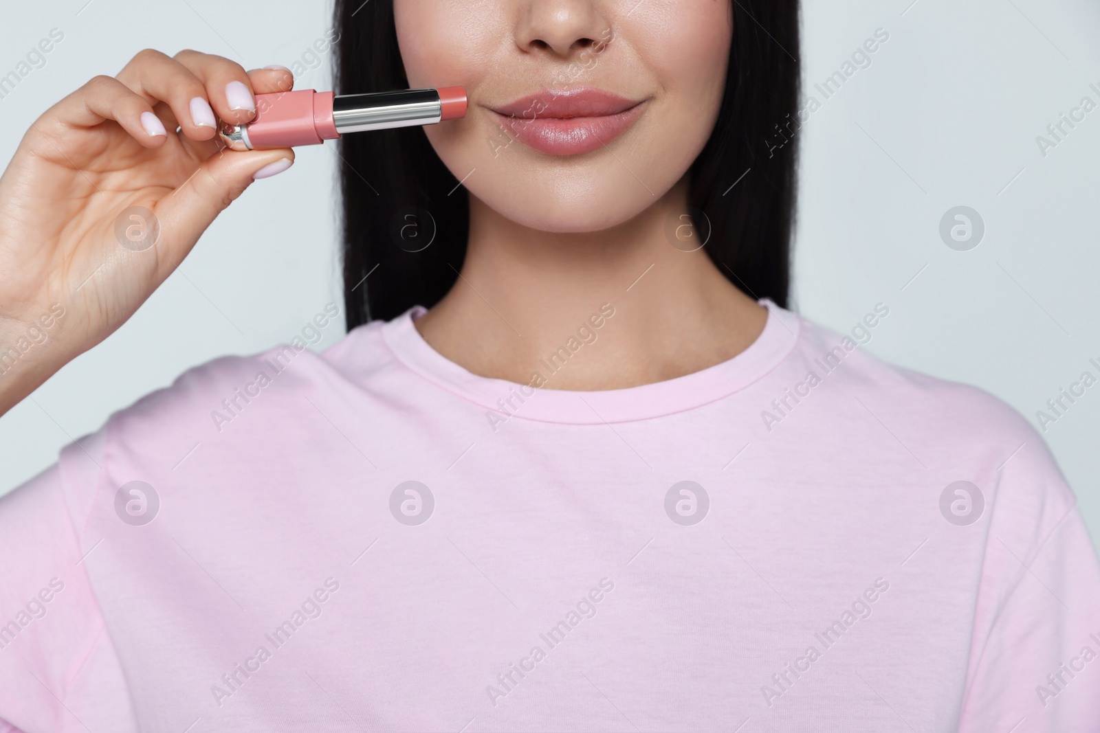 Photo of Young woman with beautiful makeup holding nude lipstick on light gray background, closeup