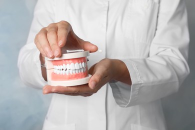 Dentist holding typodont teeth on light blue background, closeup