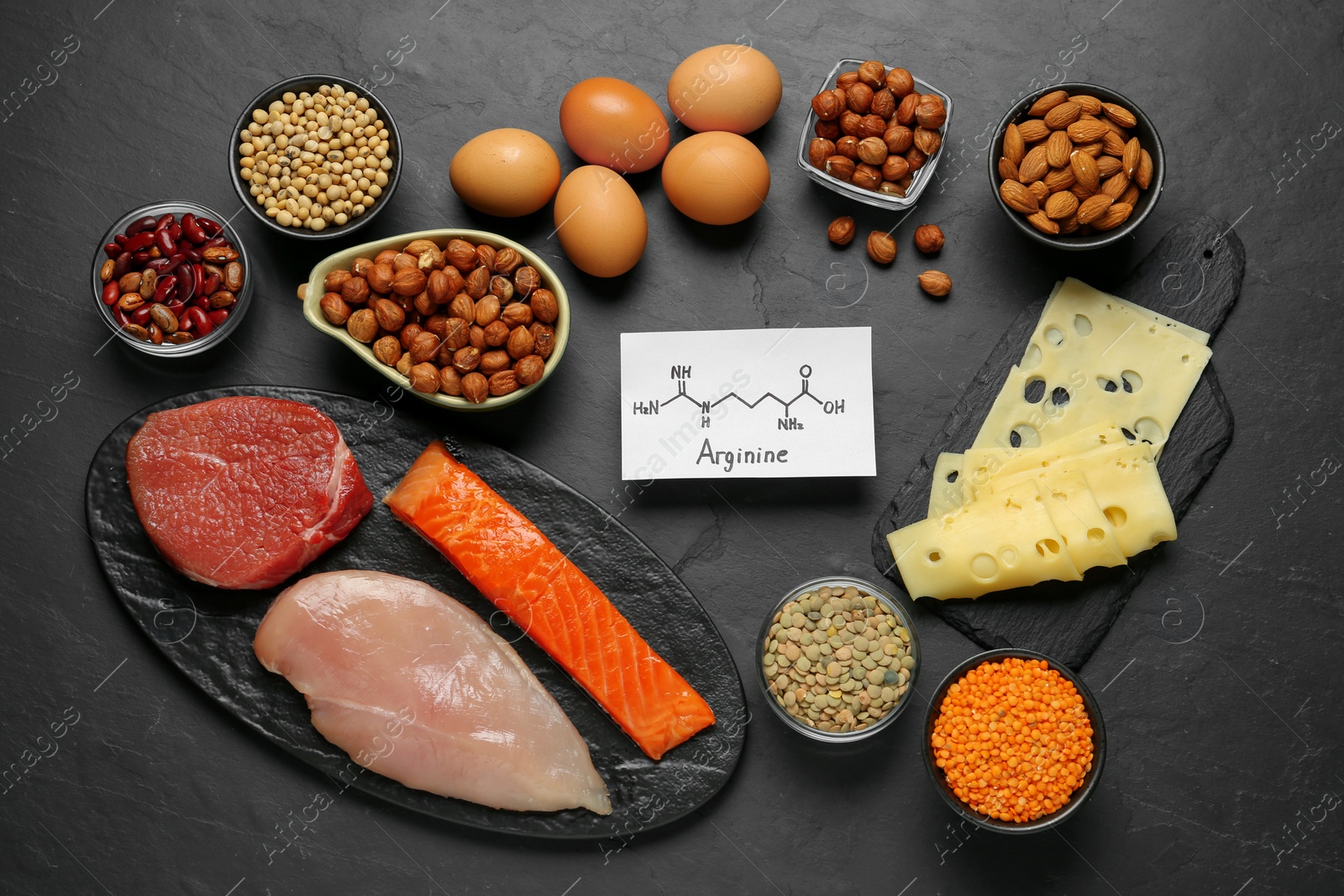 Photo of Different fresh products and paper with Arginine chemical formula on black table, flat lay. Sources of essential amino acids