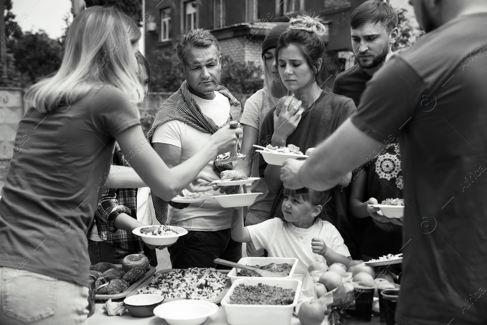 Photo of Volunteers serving food for poor people outdoors, black and white effect