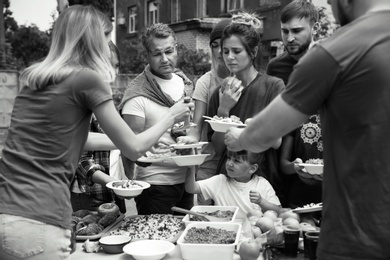 Volunteers serving food for poor people outdoors, black and white effect