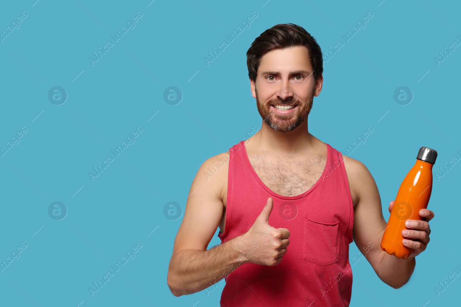 Photo of Man with orange thermo bottle showing thumbs up on light blue background. Space for text