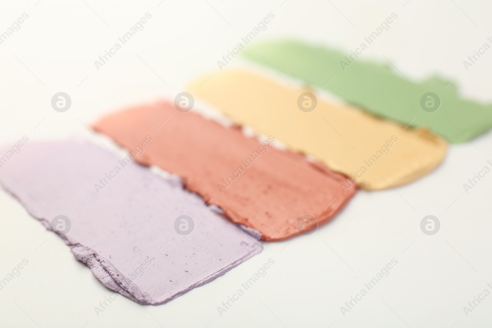 Photo of Samples of different color correcting concealers on white background, closeup