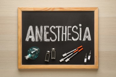 Photo of Blackboard with word Anesthesia, mask and drugs on wooden table, top view