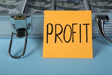 Photo of Economic profit. Note and briefcase with banknotes on light blue background, closeup
