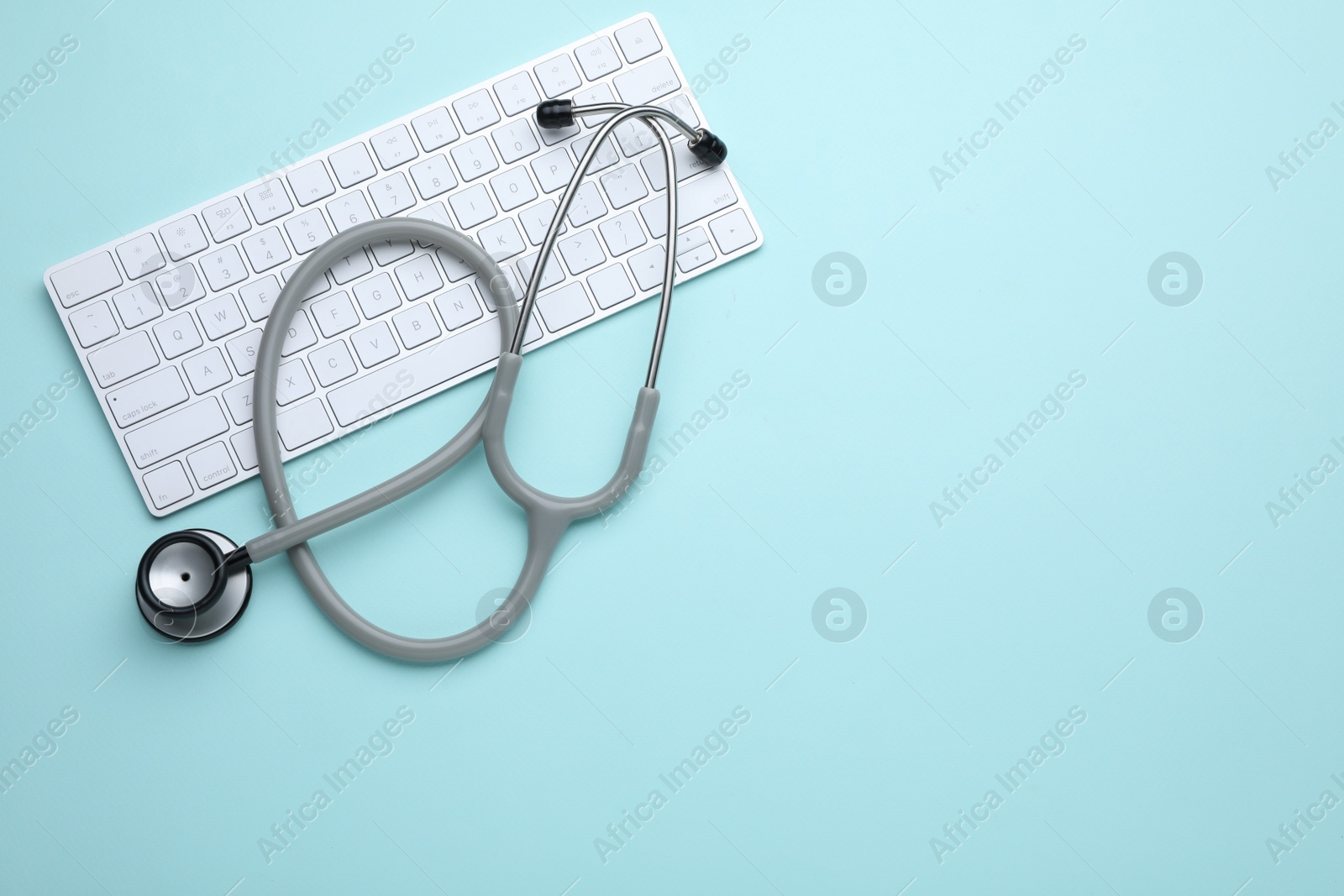 Photo of Computer keyboard with stethoscope on turquoise background, top view. Space for text