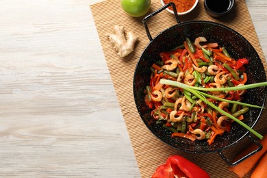 Photo of Shrimp stir fry with vegetables in wok and ingredients on wooden table, flat lay. Space for text