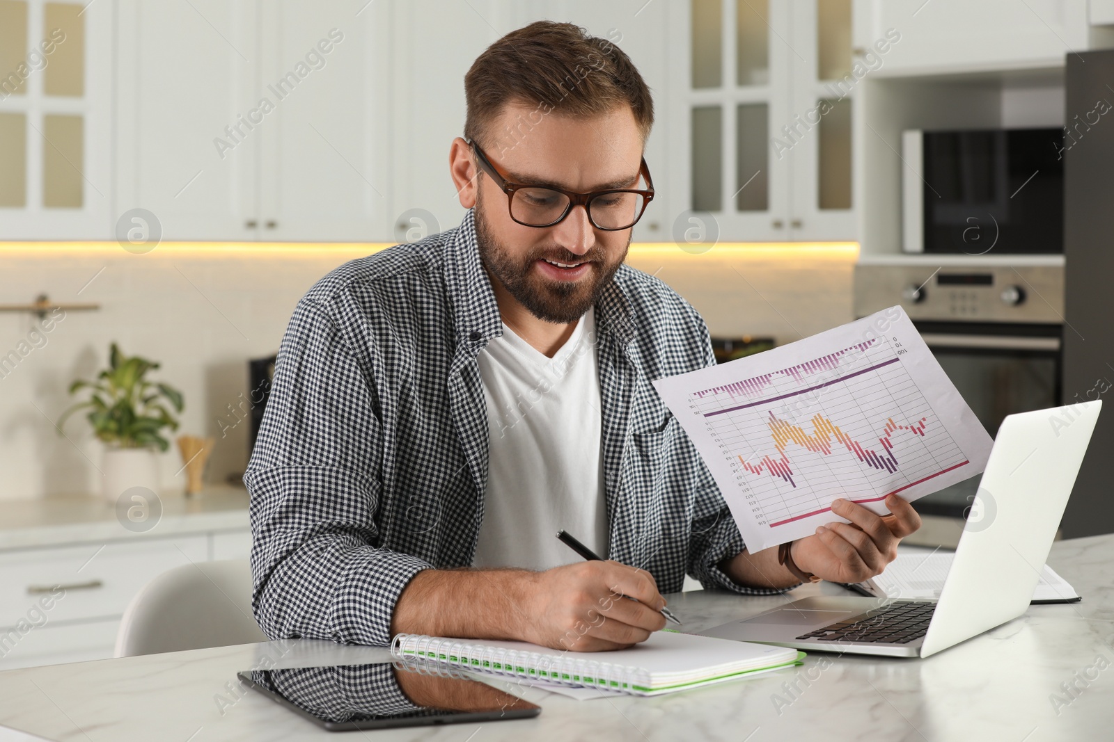 Photo of Young man working with document and laptop at home