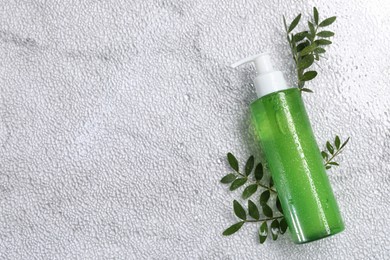 Bottle of face cleansing product and green leaves on white textured table, flat lay. Space for text