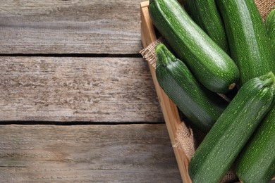 Photo of Raw ripe zucchinis in crate on wooden table, top view. Space for text