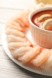 Photo of Tasty boiled shrimps with cocktail sauce and lemon on white wooden table, closeup