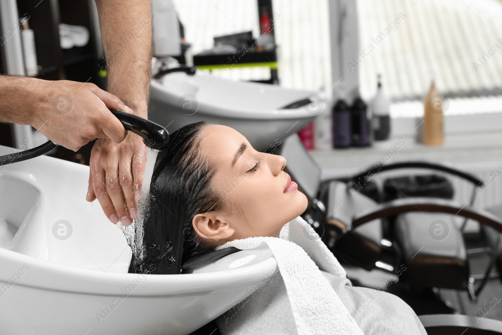 Photo of Stylist washing client's hair at sink in beauty salon