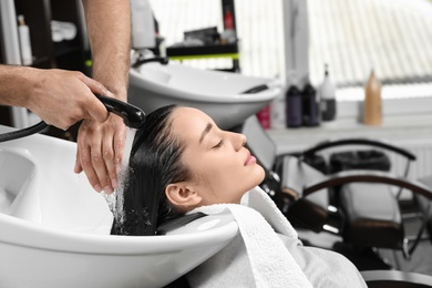 Stylist washing client's hair at sink in beauty salon