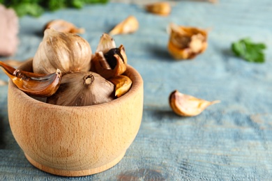 Photo of Bowl of black garlic on blue wooden table. Space for text