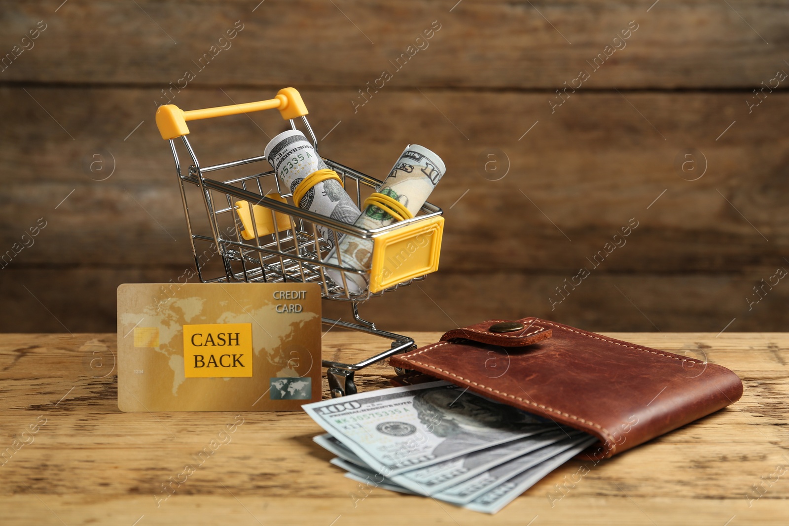 Photo of Credit card, wallet and shopping cart with dollar banknotes on wooden table. Cashback concept