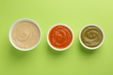 Bowls with healthy baby food on light green background, flat lay