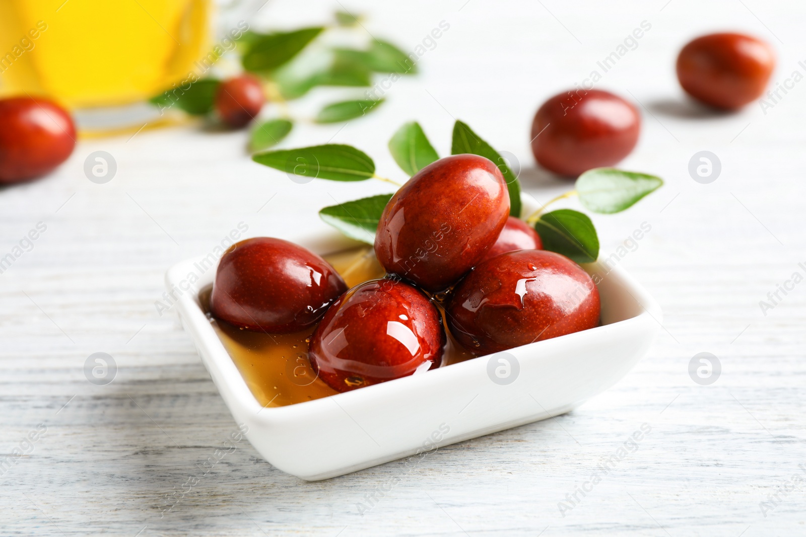 Photo of Sauce boat with jojoba oil and seeds on white wooden table