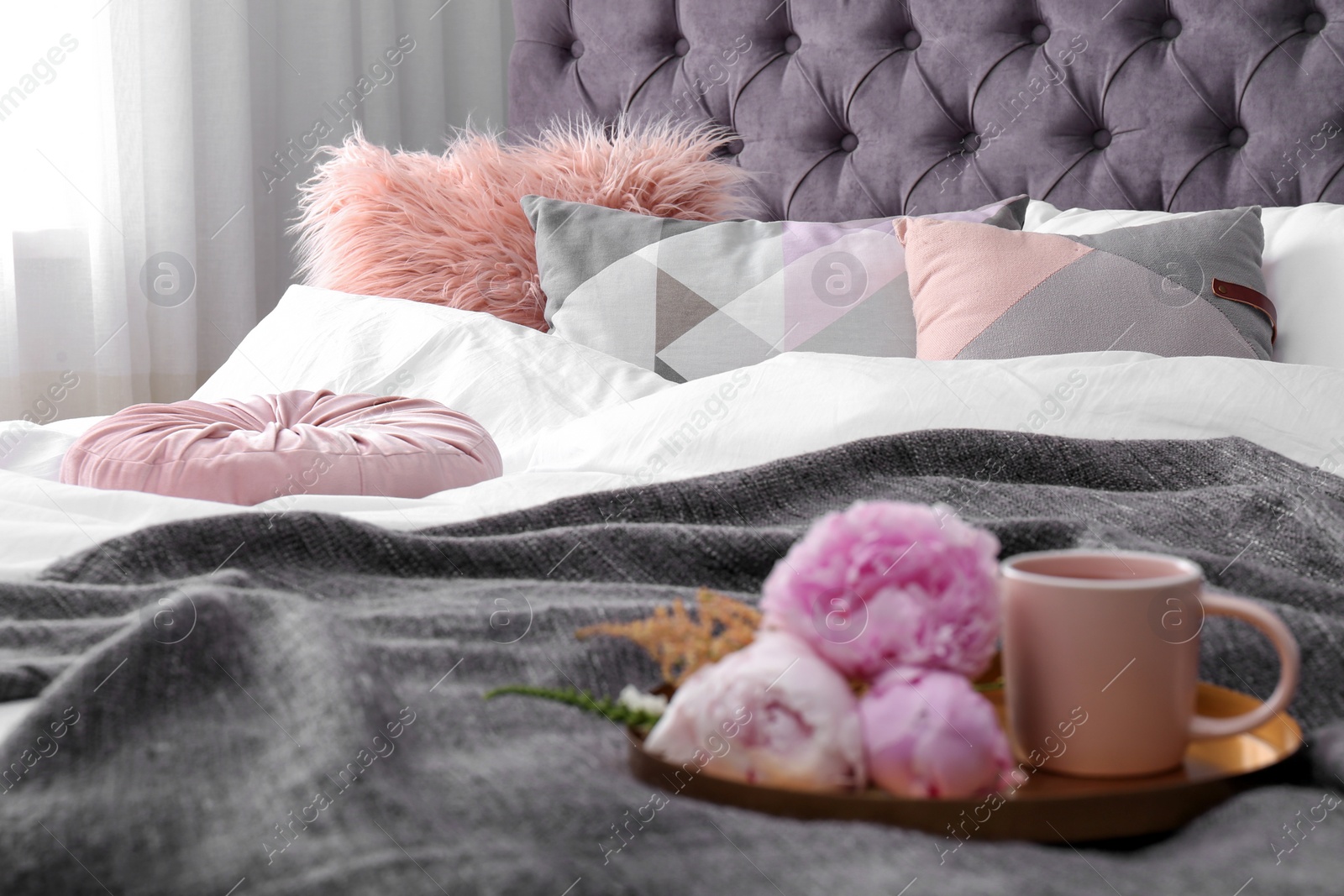 Photo of Bed with pillows, cup of drink and bouquet in room