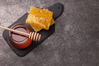 Sweet golden honey in jar, dipper and pieces of honeycomb on grey textured table, top view. Space for text