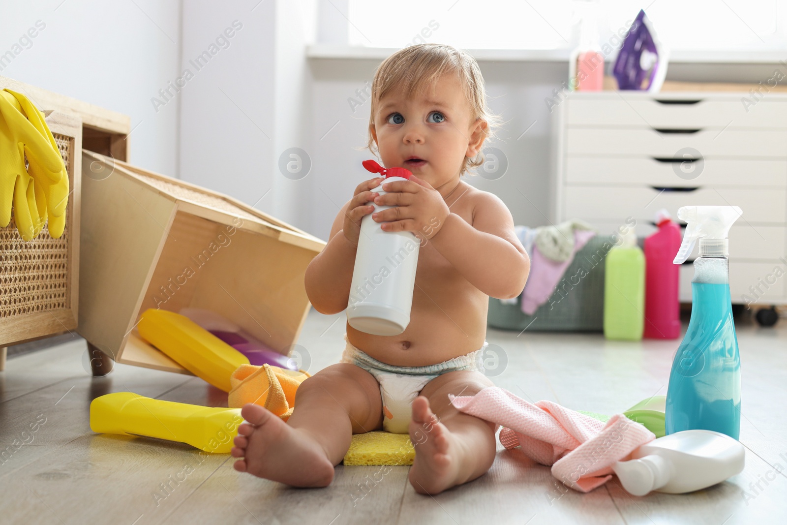 Photo of Cute baby playing with bottle of detergent on floor at home. Dangerous situation