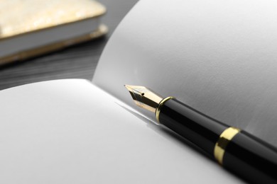 Stylish black fountain pen on open notebook, closeup. Space for text