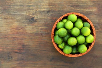 Photo of Fresh ripe limes in bowl on wooden table, top view. Space for text