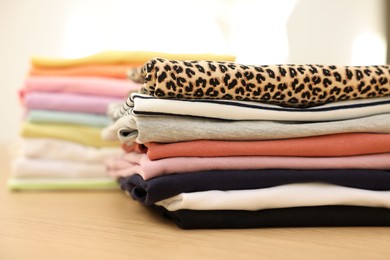 Photo of Many stacked clean clothes on wooden table, closeup