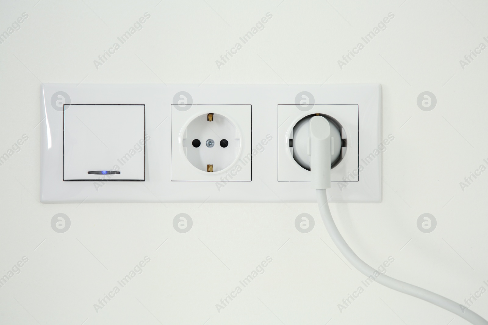 Photo of Power sockets with inserted plug and light switch on white wall indoors