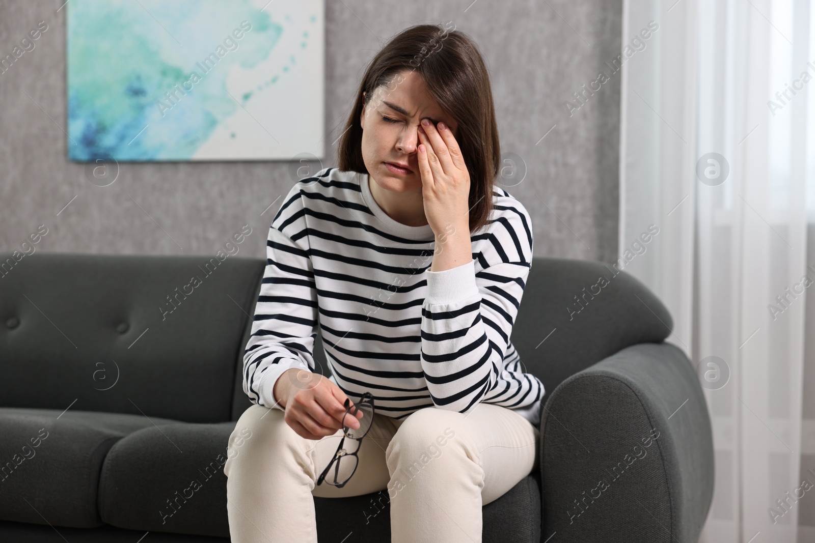 Photo of Overwhelmed woman with glasses sitting on sofa indoors