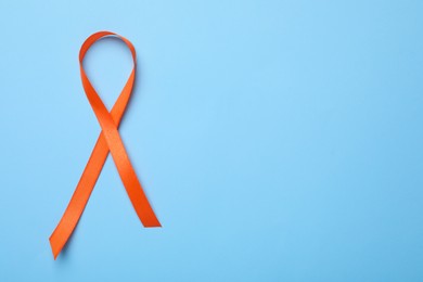 Orange ribbon on light blue background, top view with space for text. Multiple sclerosis awareness